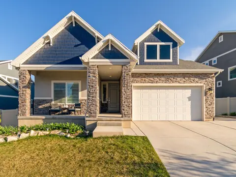 A two-story suburban home with shake siding, a stacked-stone front porch and a white double garage door under a clear blue sky